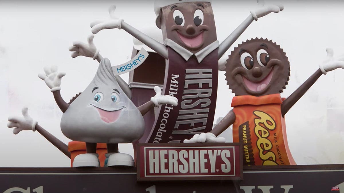 Hershey's candy mascots—Hershey's Bar, Reese's Cup, and Hershey's Kiss, inviting to learn Chocolate World History